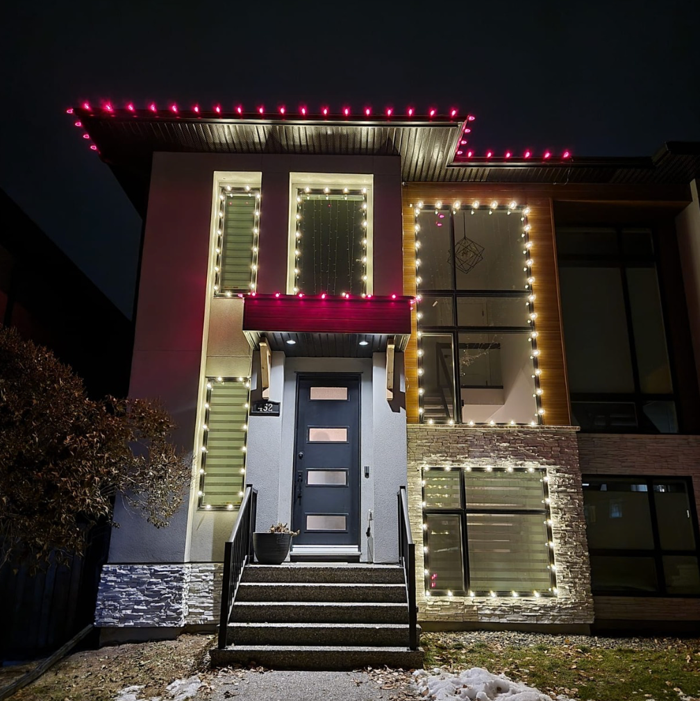Modern two-story home with roof and windows outlined in red and white holiday lighting installation at night.