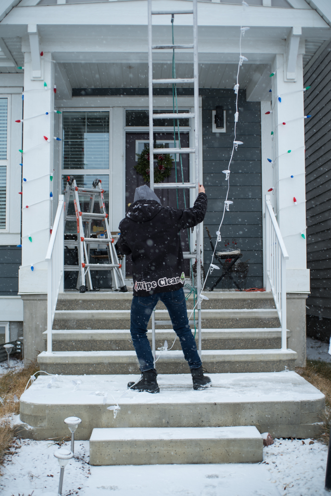A professional installer from Knight Illumination sets up holiday lights on a snowy front porch in Calgary, illustrating real-world factors behind holiday lighting cost trends and seasonal installation timing.